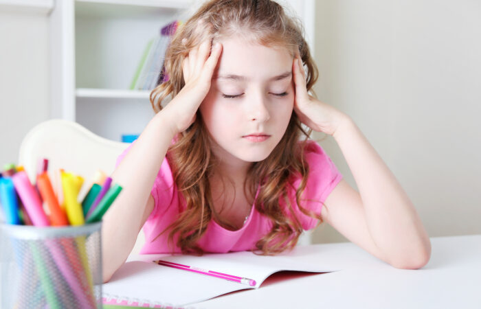 Child girl sitting at desk table learning lessons headacke.Tired kid
