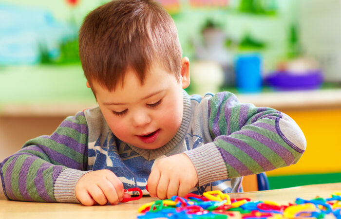 cute kid with down’s syndrome playing in kindergarten